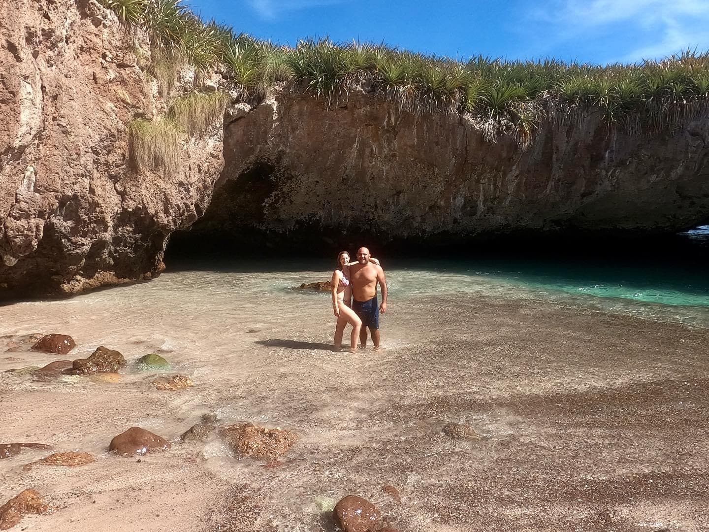 Pareja en la orilla de la Playa Escondida frente al túnel de roca por el que se entra nadando